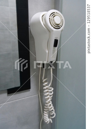 White hair dryer hanging on the wall in bathroom 129518537