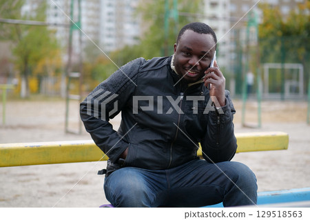African american man sits at sport ground and speaks on smartphone African american man sits at sport ground and speaks on smartphone 129518563