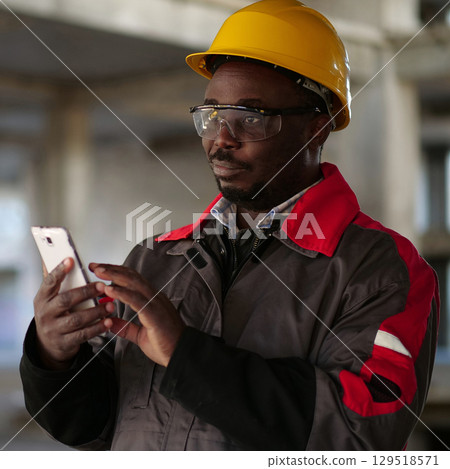 African american workman with smartphone at construction site 129518571