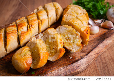 garlic bread,baguette with garlic butter and herbs, on a wooden board, with herbs and garlic cloves, 129518655