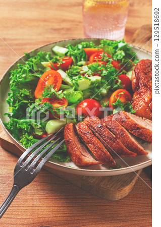 Delicious grilled duck breast served with fresh garden salad and cherry tomatoes at a rustic dining table 129518692