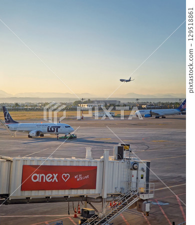 ANTALYA, TURKEY - JULY 5, 2025 Airplane landing on the tarmac at Antalya International Airport. Multiple airplanes parked and a jet bridge in the foreground, and beautiful mountains at horizon ANTALYA, TURKEY - JULY 5, 2025 Airplane landing on the tarmac at Antalya International Airport. Multiple airplanes parked and a jet bridge in the foreground, and beautiful mountains at horizon 129518861
