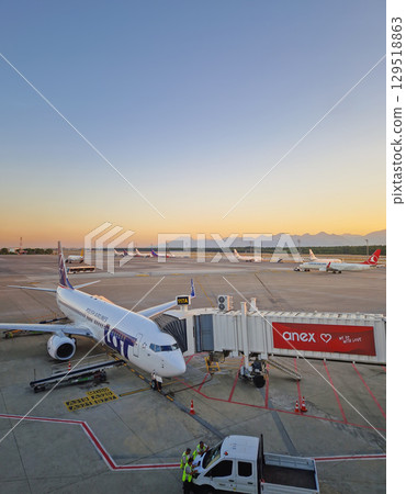 ANTALYA, TURKEY - JULY 5, 2025 Antalya airport scene at sunset and a plane docked at the jet bridge with other aircrafts visible on the tarmac. Distant mountains range silhouette in the background ANTALYA, TURKEY - JULY 5, 2025 Antalya airport scene at sunset and a plane docked at the jet bridge with other aircrafts visible on the tarmac. Distant mountains range silhouette in the background 129518863