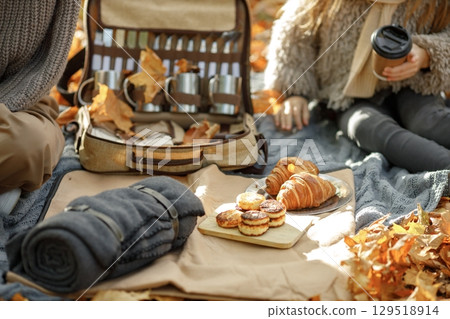 Focus on a blanket with picnic staff. Midsection of a mother and little daughter in autumn park. Woman and girl wearing grey sweaters. Focus on a blanket with picnic staff. Midsection of a mother and little daughter in autumn park. Woman and girl wearing grey sweaters. 129518914
