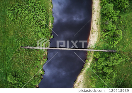 Top view of river and wooden suspension bridge in green meadow Top view of river and wooden suspension bridge in green meadow 129518989