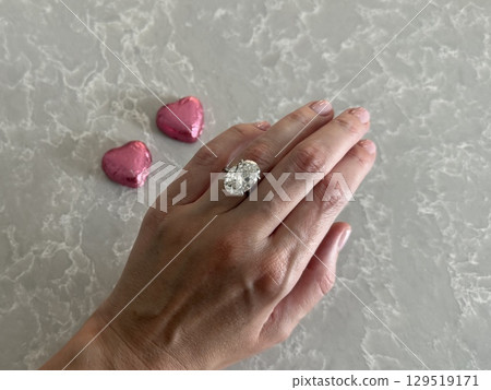 Close up of hand with oval cut diamond ring and pink hearts for Valentine's Day. Close up of hand with oval cut diamond ring and pink hearts for Valentine's Day. 129519171