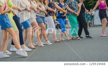 Women participants performing Bulgarian folk dance Horo in line on street, holding hands, wearing bright casual clothes, festive outdoor event. Concept of Horo dance, Bulgarian tradition 129519488