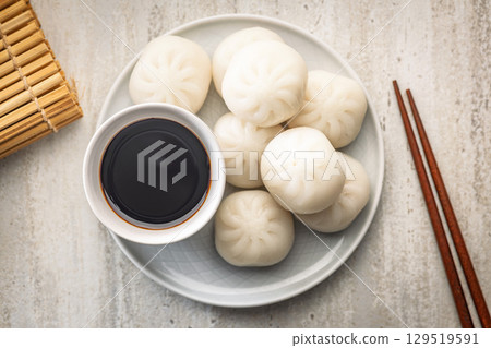 Xiao long bao. Chinese dumplings on plate and soy sauce on kitchen table. Top view. 129519591