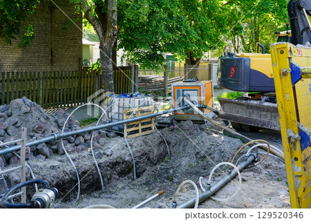 Street construction site with trenching equipment, dewatering pump, and excavator in operation 129520346
