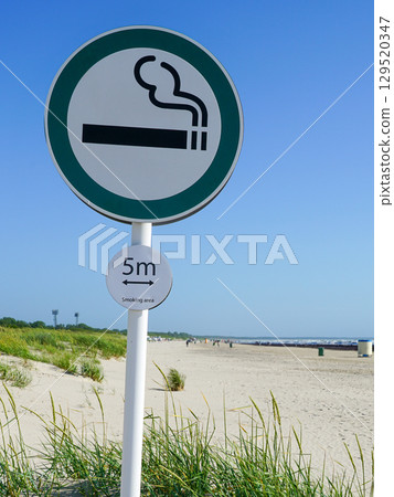 Designated Smoking Area Sign on Sandy Beach with Blue Sky and Dune Grass on a Sunny Day 129520347