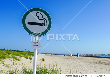 Smoking Area Sign on Sandy Beach with Sea Waves and Dune Grass Under Clear Blue Sky 129520348