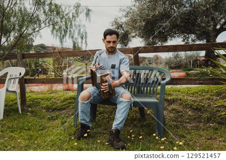 Man Playing Accordion On A Plastic Bench In The Nature Man Playing Accordion On A Plastic Bench In The Nature 129521457
