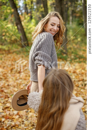 Portrait young woman holding hands with her daughter. Girl is blurred. Woman and girl wearing grey sweaters. 129521550
