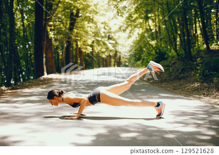 Pretty lady training in a summer park. Brunette doing yoga. Girl in a black top Pretty lady training in a summer park. Brunette doing yoga. Girl in a black top 129521628