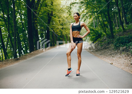 Pretty lady training in a summer park. Brunette doing yoga. Girl in a black top Pretty lady training in a summer park. Brunette doing yoga. Girl in a black top 129521629