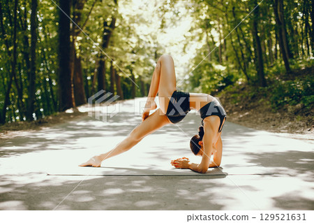 Pretty lady training in a summer park. Brunette doing yoga. Girl in a black top 129521631