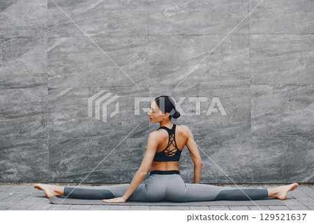 Pretty lady training in a summer city. Brunette doing yoga. Gitl in a sportsuit 129521637