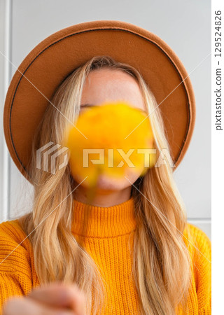 Woman faceless yellow sweater closing eyes with orange dahlia into camera Autumn Fall Bouquet for Thanksgiving holiday. Seasonal Warm colorful blossom flowers arrangement festive decoration 129524826