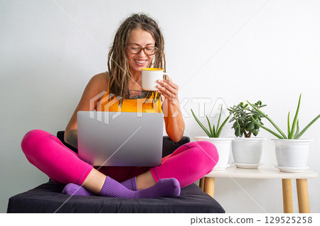 Woman with dreadlocks holds a coffee cup and uses her laptop. Woman with dreadlocks holds a coffee cup and uses her laptop. 129525258