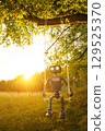 Happy humanoid robot swings among the wildflowers at sunset. Robotic object experiences feelings and emotions. Concept of technology development in the form of artificial intelligence. 129525370
