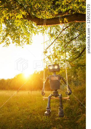 Happy humanoid robot swings among the wildflowers at sunset. Robotic object experiences feelings and emotions. Concept of technology development in the form of artificial intelligence. Happy humanoid robot swings among the wildflowers at sunset. Robotic object experiences feelings and emotions. Concept of technology development in the form of artificial intelligence. 129525370