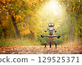 Happy humanoid robot rides a bicycle along the autumn alley. Robotic object experiences feelings and emotions. Concept of technology development in the form of artificial intelligence. 129525371