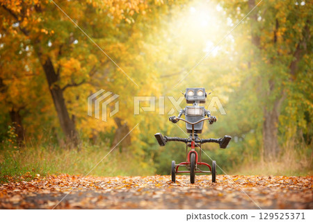Happy humanoid robot rides a bicycle along the autumn alley. Robotic object experiences feelings and emotions. Concept of technology development in the form of artificial intelligence. 129525371