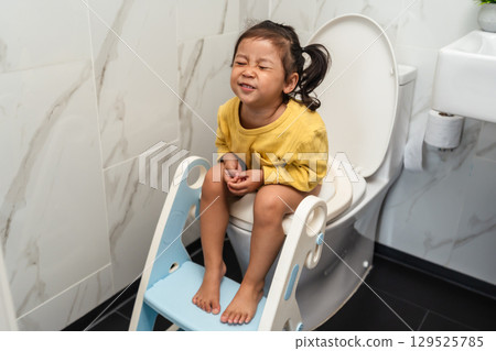 toddler girl sitting on toilet at home and suffering from stomachache and constipation toddler girl sitting on toilet at home and suffering from stomachache and constipation 129525785