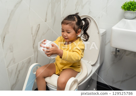 happy toddler girl is sitting on toilet with tissue at home. potty training and learning happy toddler girl is sitting on toilet with tissue at home. potty training and learning 129525786