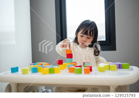 toddler girl playing block toy to stacks building cubes on table toddler girl playing block toy to stacks building cubes on table 129525793