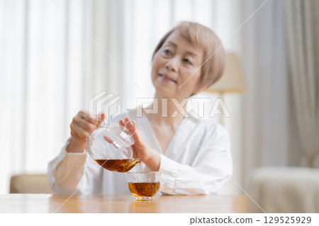 Senior woman pouring tea in the dining room Senior woman pouring tea in the dining room 129525929