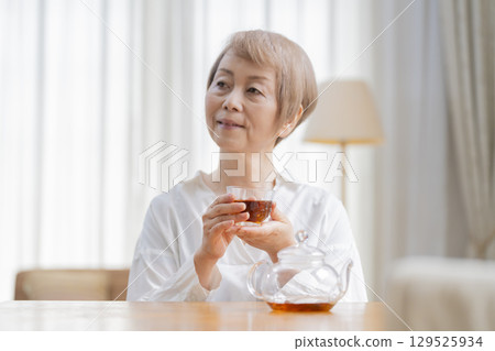 Senior woman pouring tea in the dining room Senior woman pouring tea in the dining room 129525934