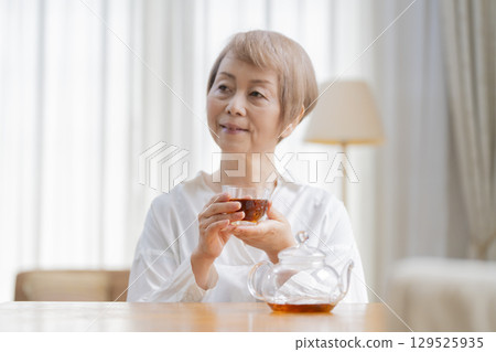 Senior woman pouring tea in the dining room Senior woman pouring tea in the dining room 129525935