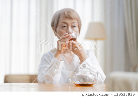 Senior woman pouring tea in the dining room Senior woman pouring tea in the dining room 129525939