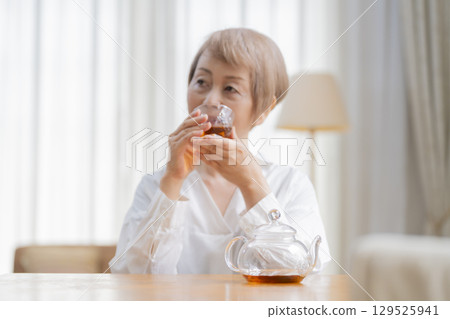 Senior woman pouring tea in the dining room Senior woman pouring tea in the dining room 129525941