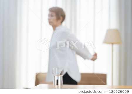 Senior woman stretching and drinking water in the living room Senior woman stretching and drinking water in the living room 129526009