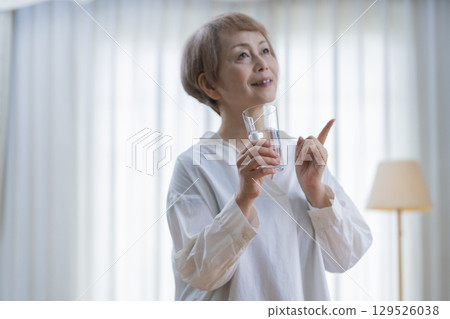 老年婦女在客廳伸展身體和喝水 129526038