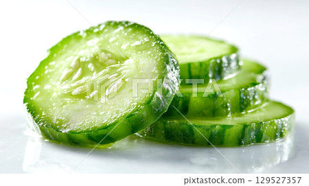 Fresh cucumber slices glistening on bright surface, showcasing their vibrant green color and juicy texture 129527357