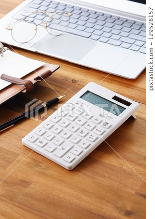 Image of a business person doing desk work with a laptop, notebook, and calculator spread out on a desk Image of a business person doing desk work with a laptop, notebook, and calculator spread out on a desk 129528157