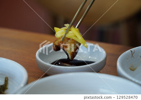 Close-Up of Grilled Eel Dipped in Sauce with Chopsticks 129528470