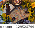 Mystic still life with decorated magic book of spells, tarot card, tansy flowers, crystals, black candles and witchy ritual objects on old table. Occult, esoteric and wicca concept Mystic still life with decorated magic book of spells, tarot card, tansy flowers, crystals, black candles and witchy ritual objects on old table. Occult, esoteric and wicca concept 129528799