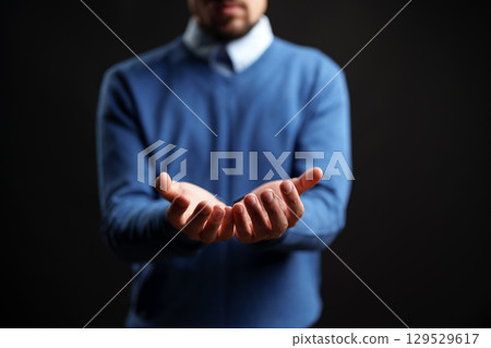 Man extending hands in a welcoming gesture against a dark background during a studio session 129529617