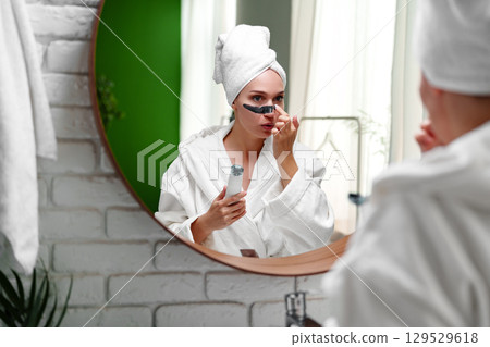 Woman applying facial treatment in a modern bathroom reflecting self-care routine and skincare focus 129529618
