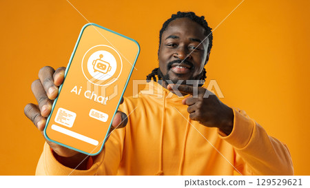 Young man excitedly shows smartphone screen displaying AI chat interface in bright orange setting Young man excitedly shows smartphone screen displaying AI chat interface in bright orange setting 129529621