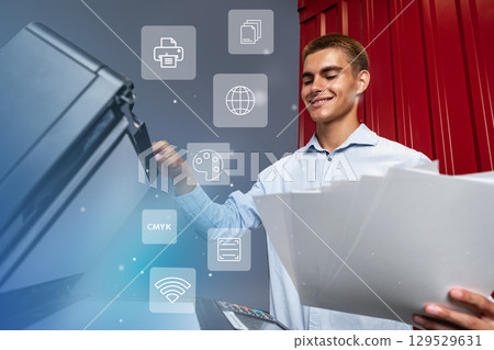 Young man using a multifunction printer to copy documents in an office setting during daytime 129529631