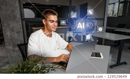 Engaged young man working on laptop in modern office with AI technology representation 129529649