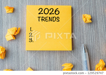 2026 Trends word on yellow note with pen and crumbled paper on wooden table background. New Year New Start, Resolutions, Strategy and Goal concept 129529747
