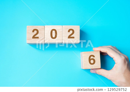hand holding wooden cube block with 2026 text on blue background. Resolution, plan, review, goal, start and New Year holiday concepts 129529752