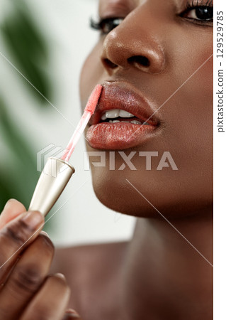 Woman applying lip gloss in a beauty routine at home during the day with plants in the background 129529785