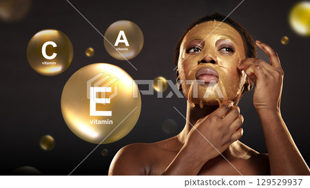 Woman applying gold face mask enriched with vitamins C and E for skincare at home in a serene, dimly lit environment 129529937